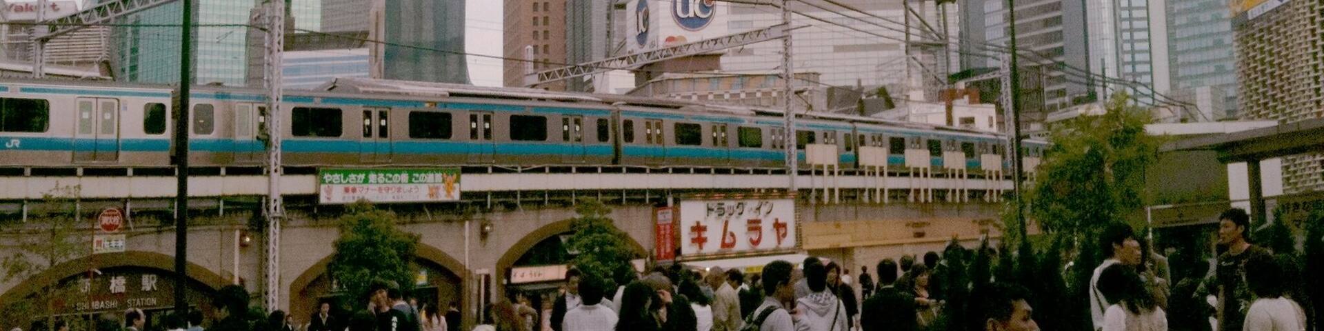 A busy urban scene with a train passing over a bridge, surrounded by modern skyscrapers and a crowd of people.