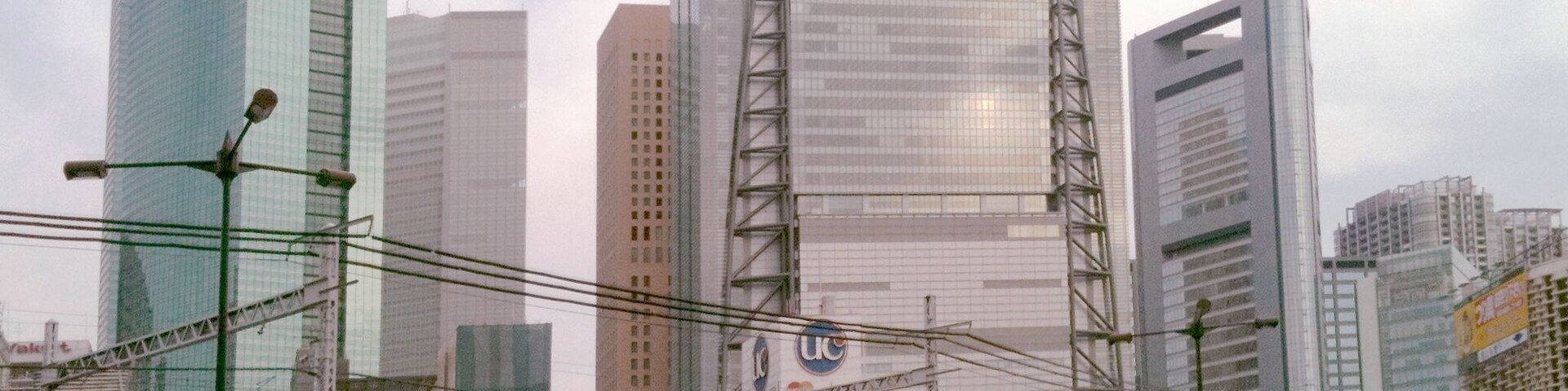 Cena urbana movimentada com um trem cruzando uma ponte, cercada por arranha-céus modernos e uma multidão de pessoas.