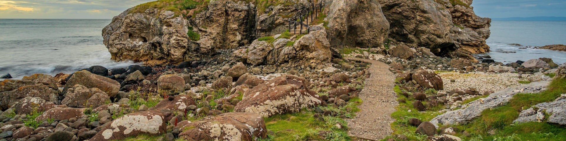 A rocky coastal landscape with a ruined stone structure and a gravel path leading to it.
