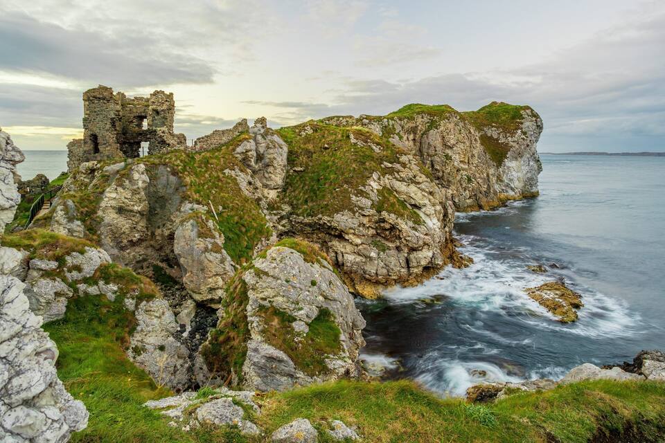 Rugged coastal cliffs with remnants of stone walls and a flowing river.
