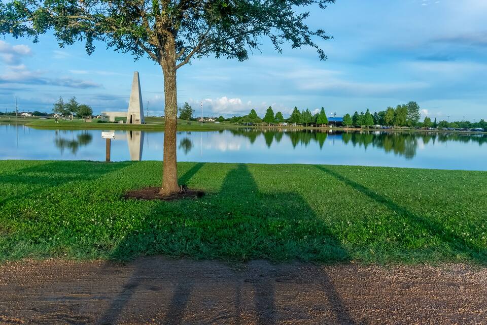 A calm lake with a grassy area, a tree, and a monument in the background.