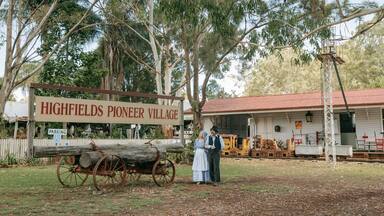 A sign for Highfields Pioneer Village, a rustic building, and a vintage cart.