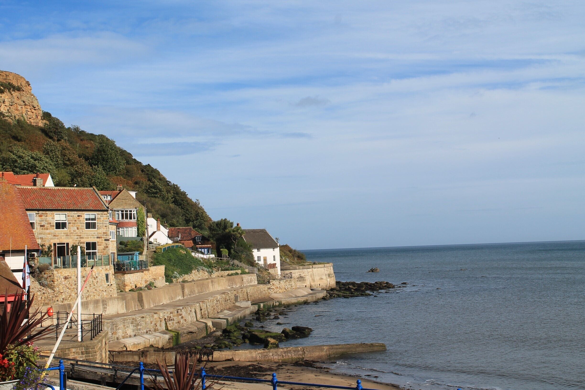 A coastal town with stone houses, a cliff, and a rocky shoreline.