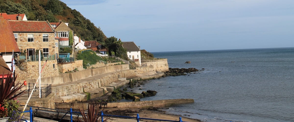 A coastal town with stone houses, a cliff, and a rocky shoreline.