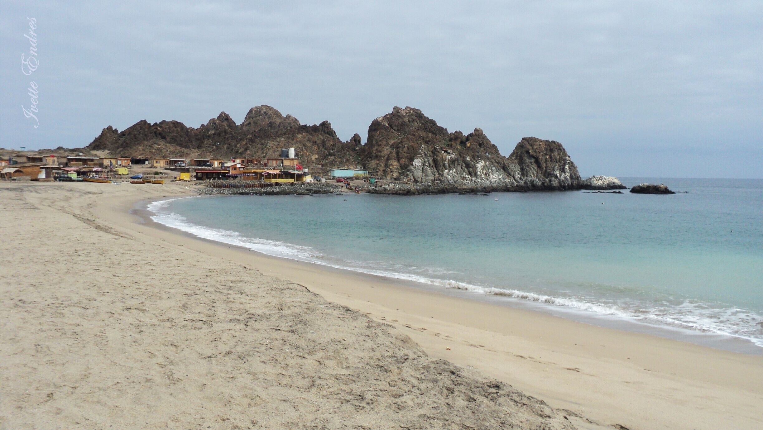 A sandy beach with a rocky coastline and buildings in the background.