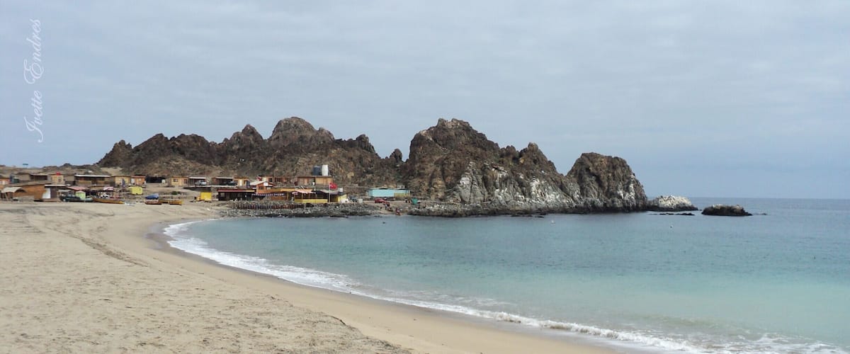 A sandy beach with a rocky coastline and buildings in the background.