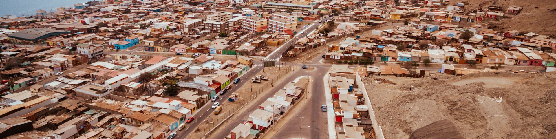Vista aérea de uma cidade costeira com edifícios bem próximos, uma avenida principal e montanhas ao fundo.
