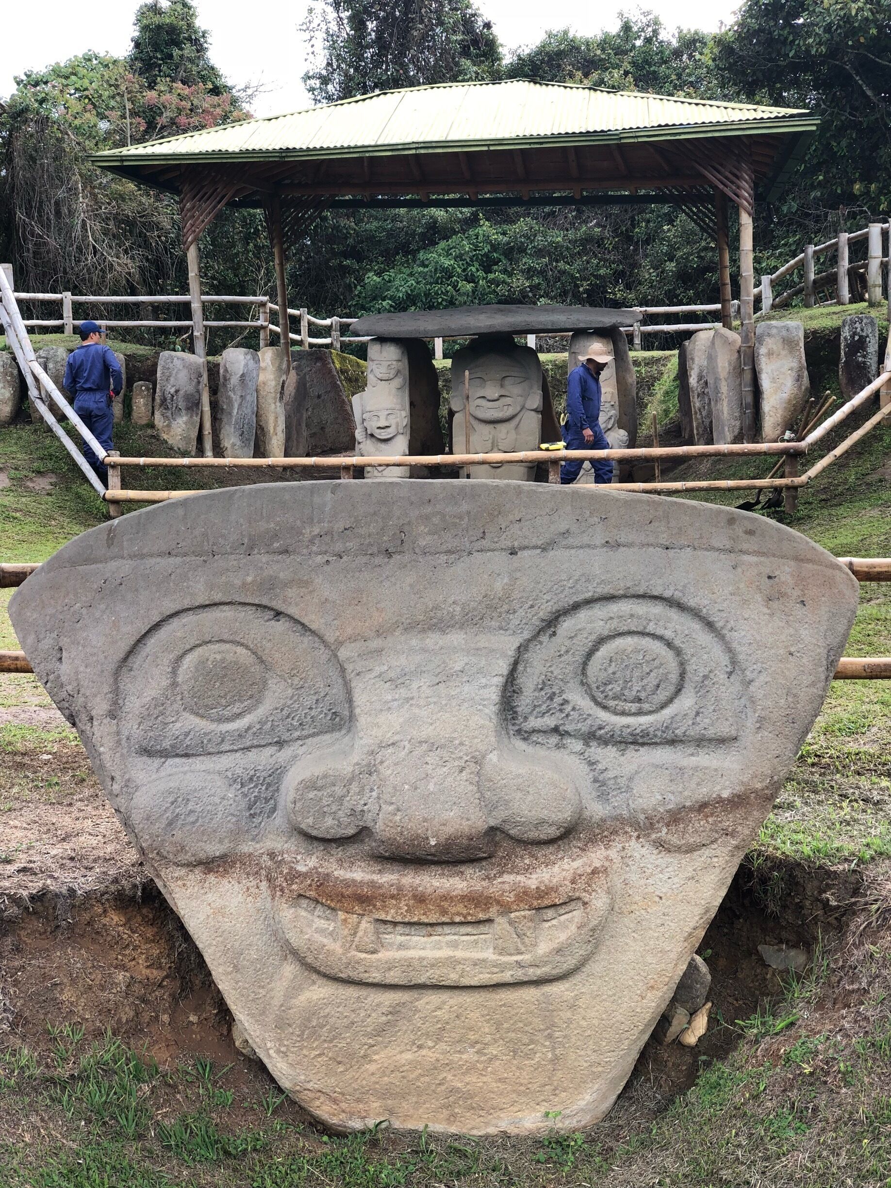A large stone face sculpture in a park with a covered viewing area and stone pillars in the background.