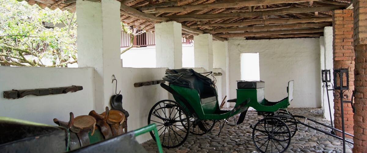 A traditional wooden structure with a thatched roof, stone flooring, and a green carriage.