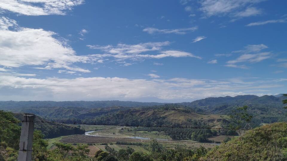 A mountainous landscape with a river, dense vegetation, and a clear sky.