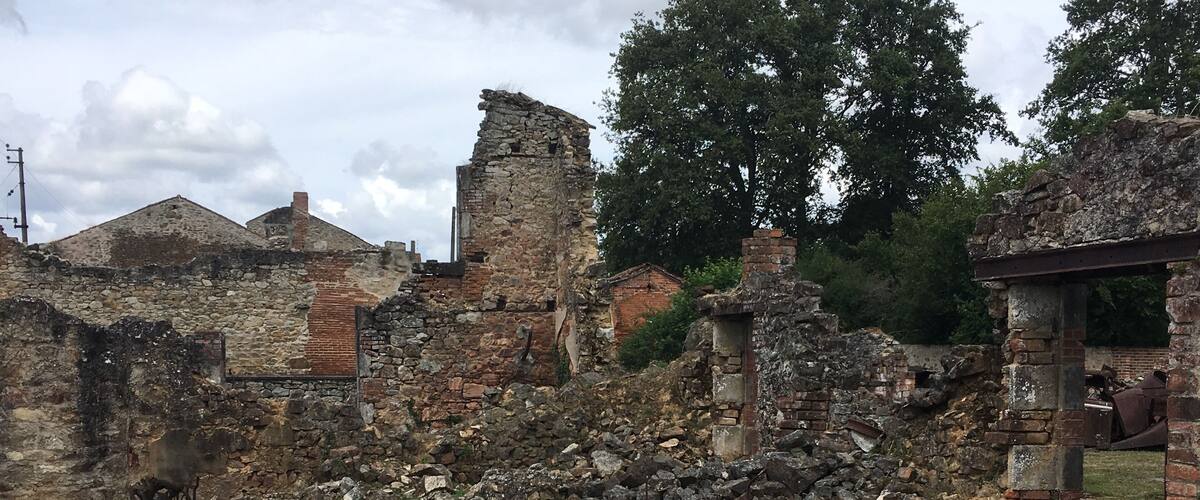 An abandoned historical site with stone walls, rusted metal objects, and overgrown vegetation.