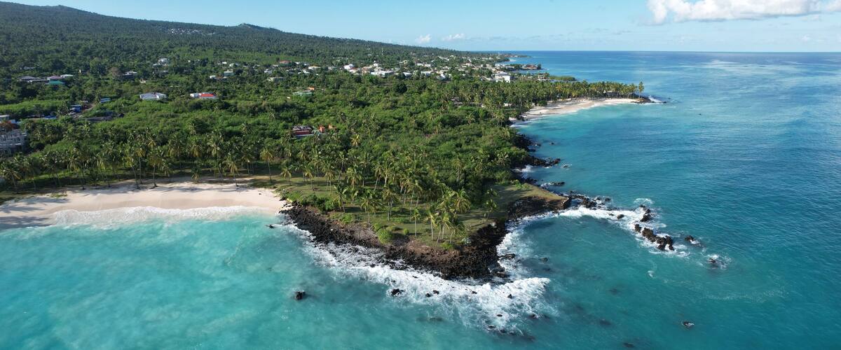 A coastal town with a beach, dense greenery, and a clear blue sea.