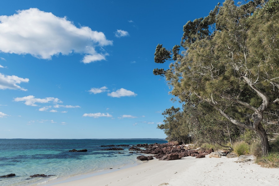 Une plage à l’eau turquoise et limpide, au sable blanc, et parsemée de formations rocheuses.