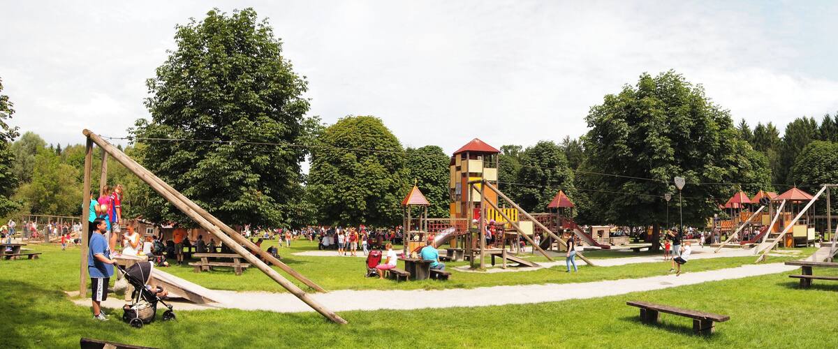 A playground with slides, swings, and picnic tables in a park.