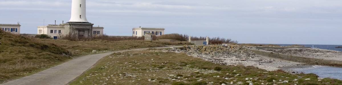 A lighthouse with the inscription "SEIN" on its tower, a pathway leading to it, and a rocky shoreline in the background.