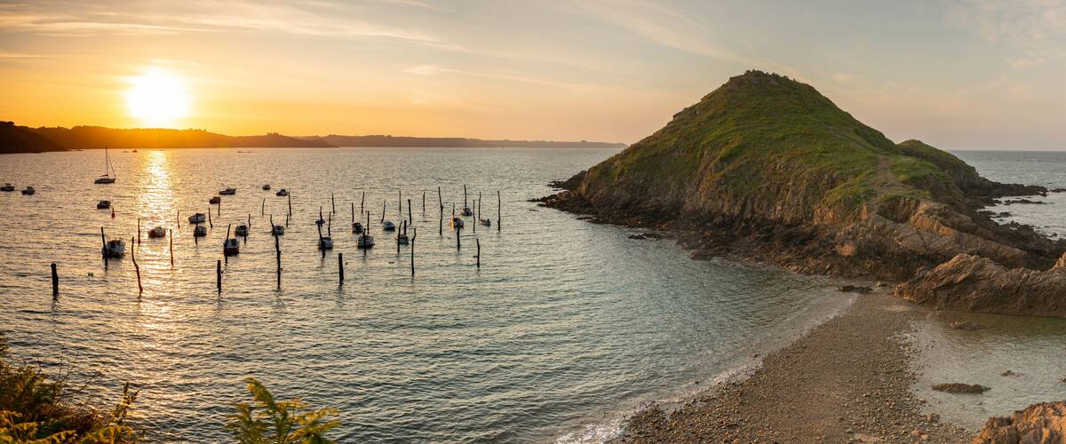 A coastal landscape with a prominent hill, calm sea, and several anchored boats.