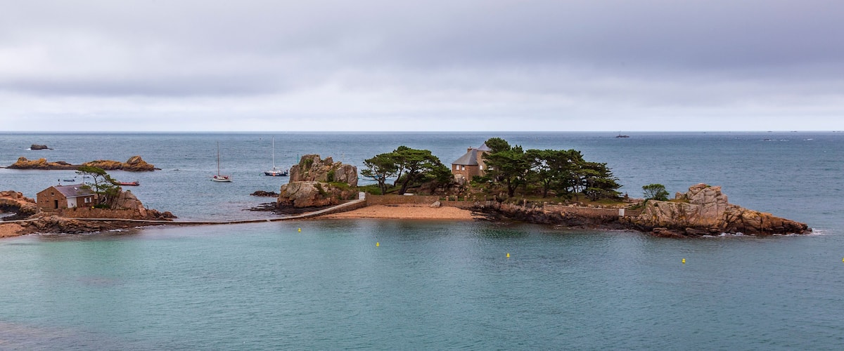 A coastal landscape with rocky outcrops, a small building, and a clear view of the sea.