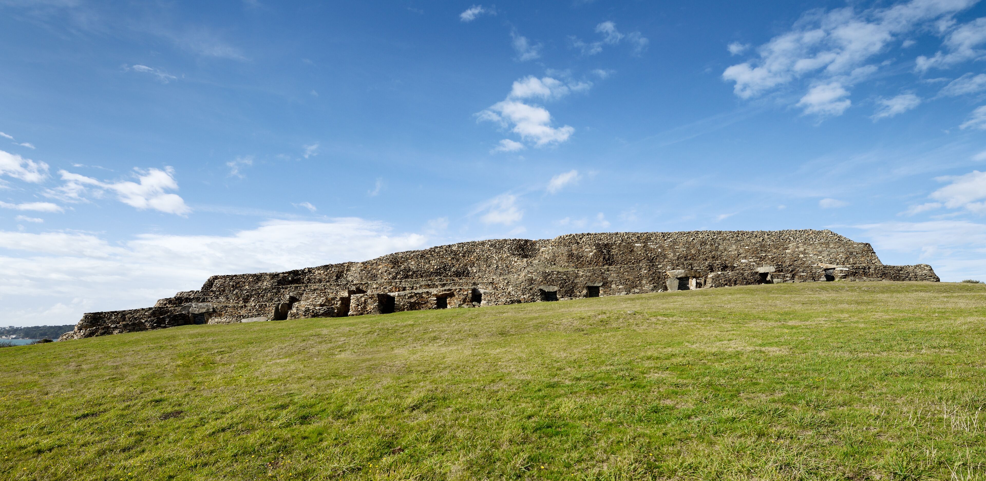 A large stone structure on a grassy hill with a clear blue sky.
