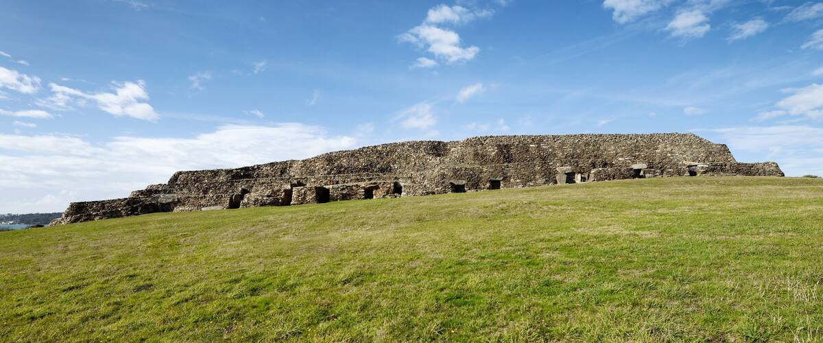 A large stone structure on a grassy hill with a clear blue sky.
