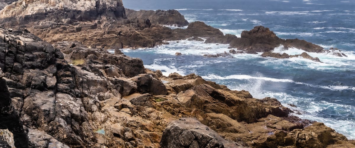 Rugged coastal cliffs with a castle ruin and turbulent ocean waves.