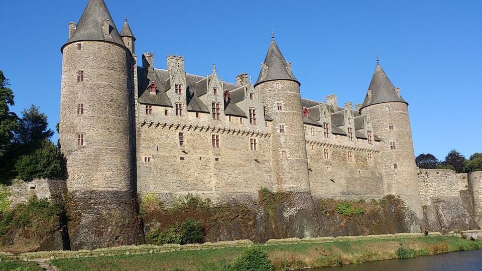 A historic castle with multiple towers, a moat, and a river in the foreground.