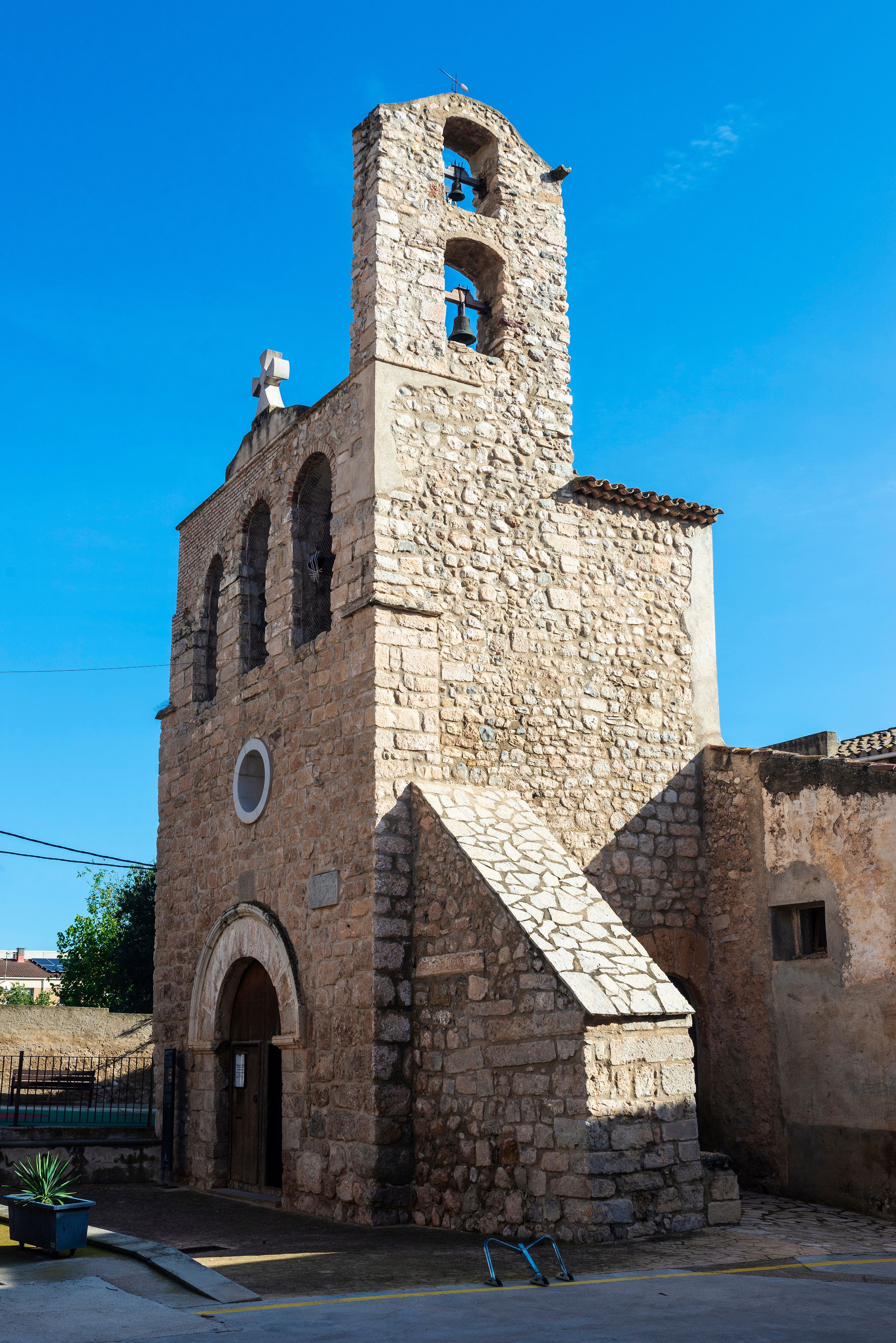 Une église en pierre dotée d’un clocher, de fenêtres en arc de cercle et d’une croix au sommet.