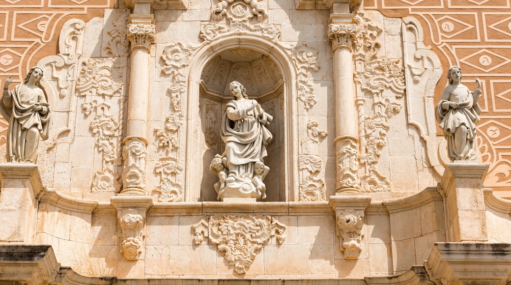 En detaljeret facade på en historisk bygning med udsmykkede udskæringer, statuer og en midterliggende arkade.