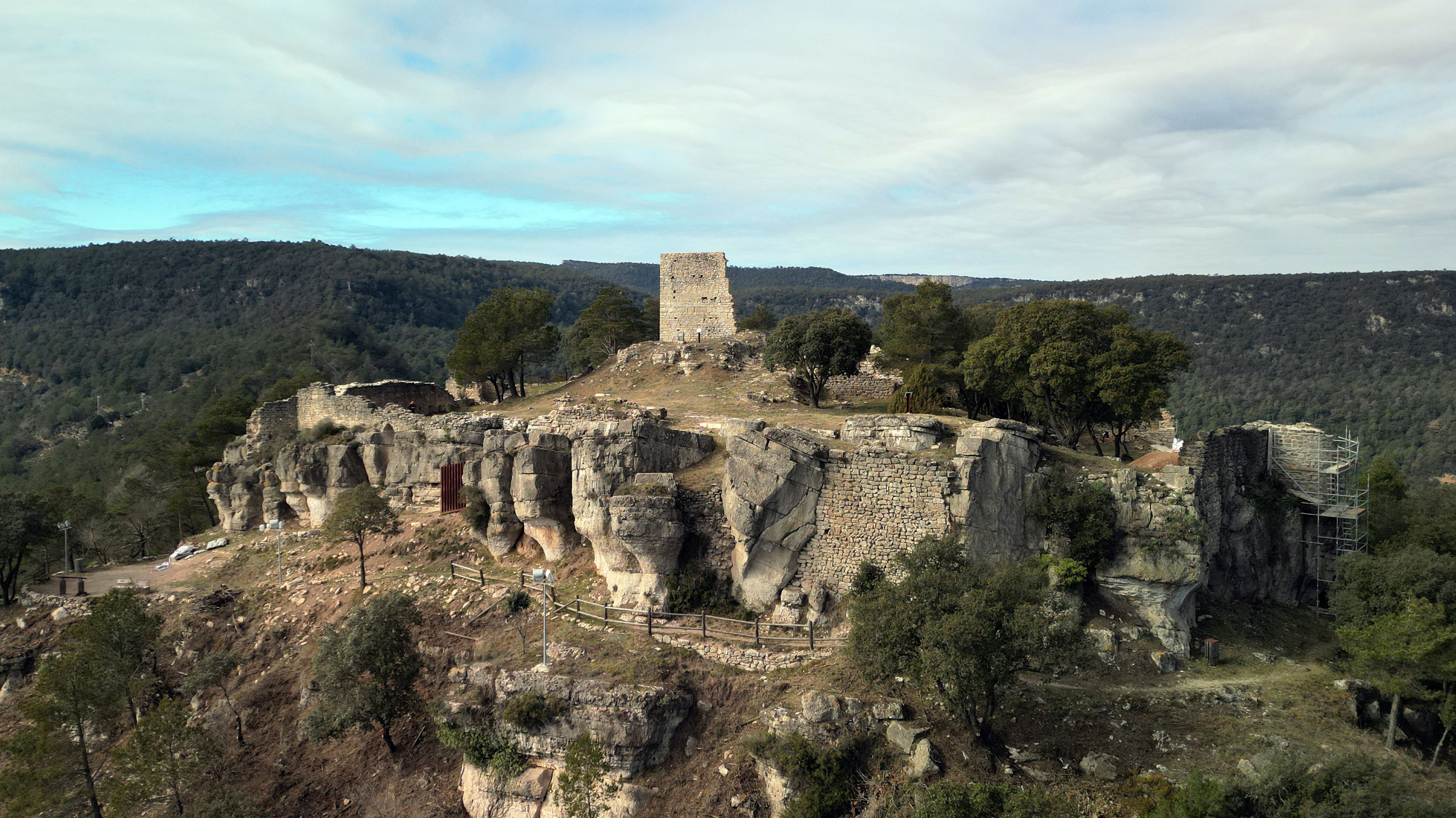 A historical stone tower on a hilltop with surrounding rocky terrain and trees.