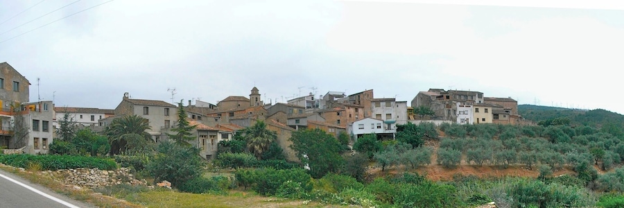 Un pueblo en la ladera con casas de piedra tradicionales, olivares y una carretera en primer plano.