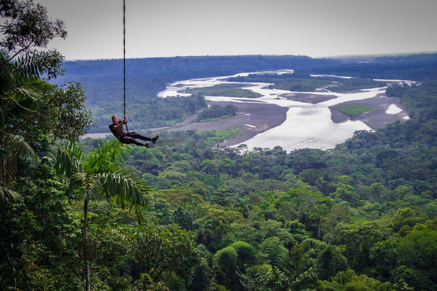 Tourist having fun in the air held by a rope. Fabulous Amazonian landscape where you can appreciate the immensity of the jungle and a huge river.