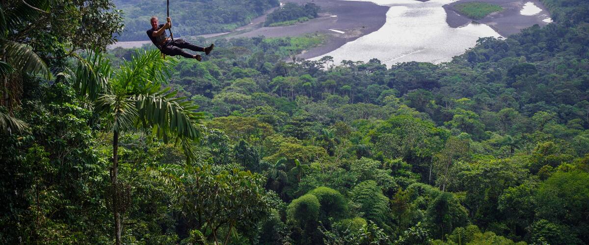A person bungee jumping from a high cliff over a lush green forest with a river below.