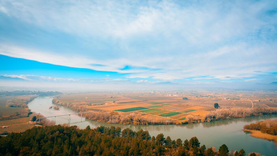 A river winding through a valley with fields and a bridge.