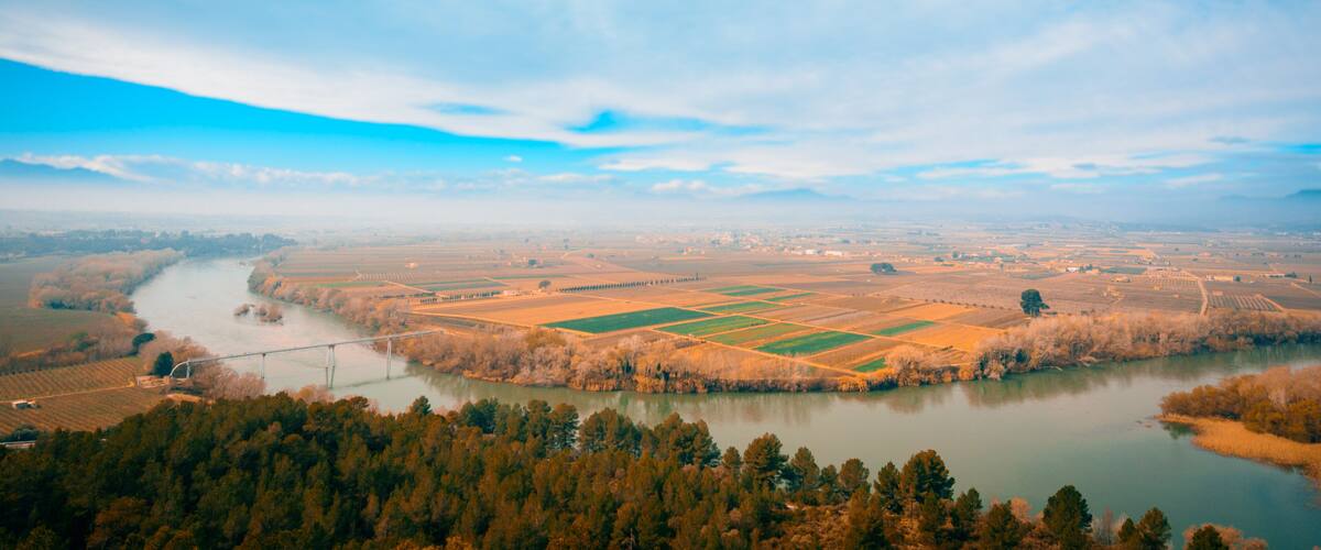 A river winding through a valley with fields and a bridge.
