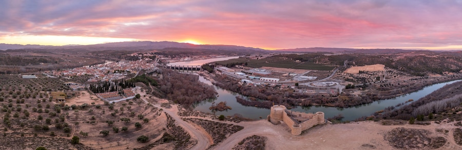 Un valle fluvial con un puente, un castillo y un pueblo con edificios y campos.