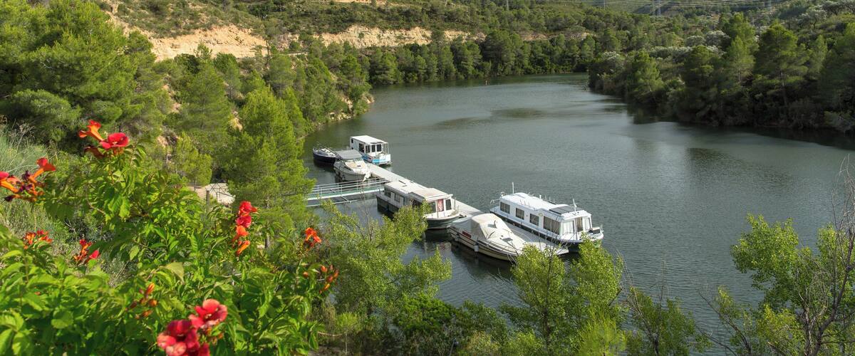 A river with boats docked, surrounded by green hills and trees.
