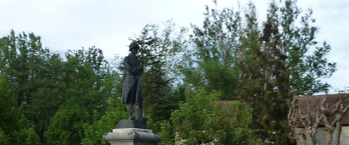 A statue on a pedestal in a park with trees and a building in the background.