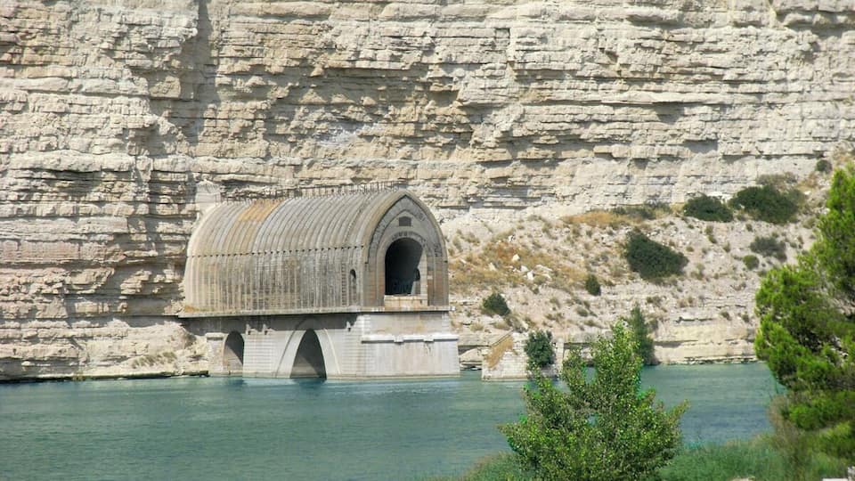 A stone bridge with a covered passageway over a body of water, set against a backdrop of layered rock cliffs.
