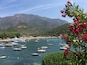 A coastal bay with numerous boats, a sandy beach, and a mountainous backdrop.