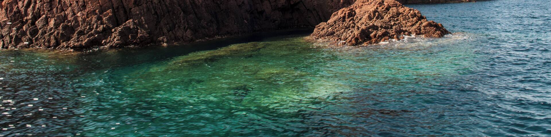 A rocky coastline with clear turquoise waters and a grassy hill in the background.