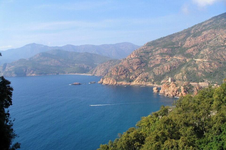 Paisagem costeira com mar azul cristalino, falésias rochosas e um pequeno barco.