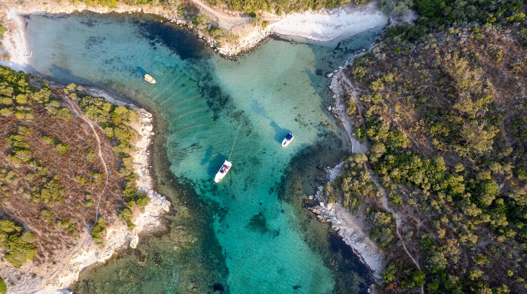 An aerial view of a coastal area with clear turquoise waters, rocky shorelines, and a few boats.