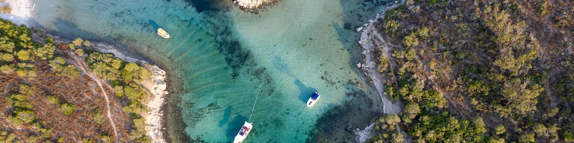 An aerial view of a coastal area with clear turquoise waters, rocky shorelines, and a few boats.