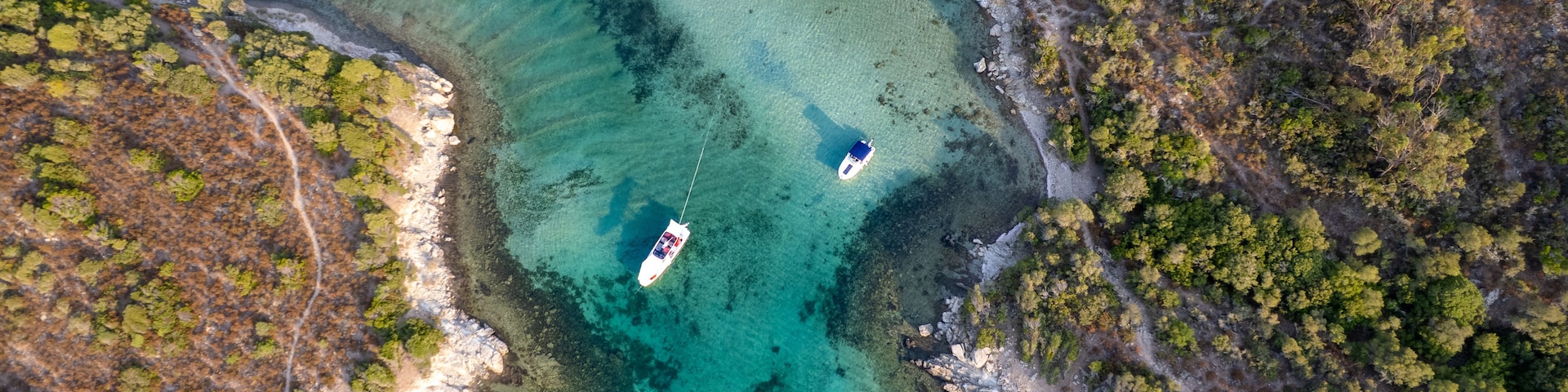Eine Luftaufnahme einer Küstenlandschaft mit klarem türkisblauem Wasser, felsigen Ufern und einigen Booten.