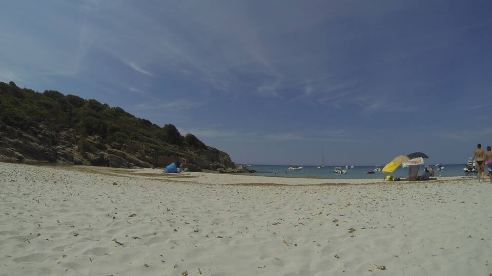 A sandy beach with a rocky cliff, a blue tent, and a yellow umbrella.