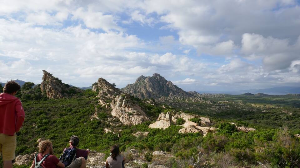 A group of people on a rocky hill overlooking a mountainous landscape with green vegetation and rocky outcrops.