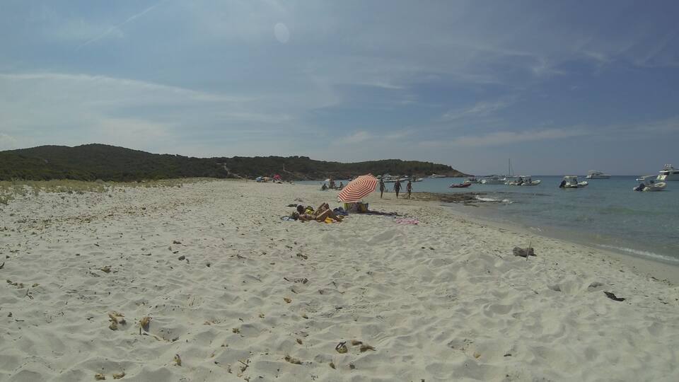 A sandy beach with a few people, a striped umbrella, and boats in the water.