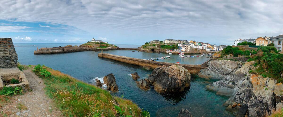 A coastal town with a stone lighthouse, harbor, and buildings along the cliffs.