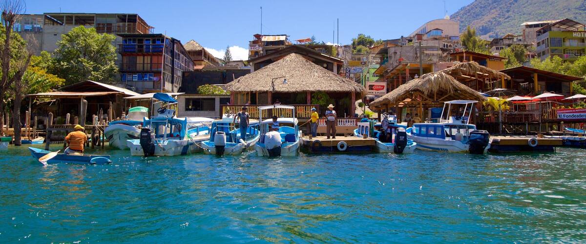 A coastal town with boats docked along the shore, surrounded by buildings and a mountain in the background.