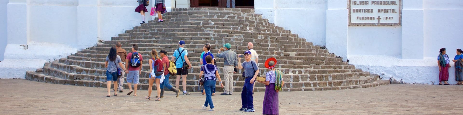 A church with purple drapes, a stone staircase, and a sign reading "Ilesia Parroquial Santiago Apostol Fundada 1947".