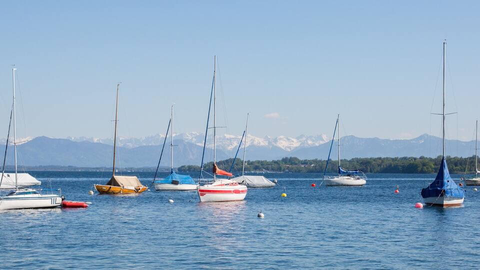 A calm lake with several sailboats anchored, surrounded by mountains and clear skies.